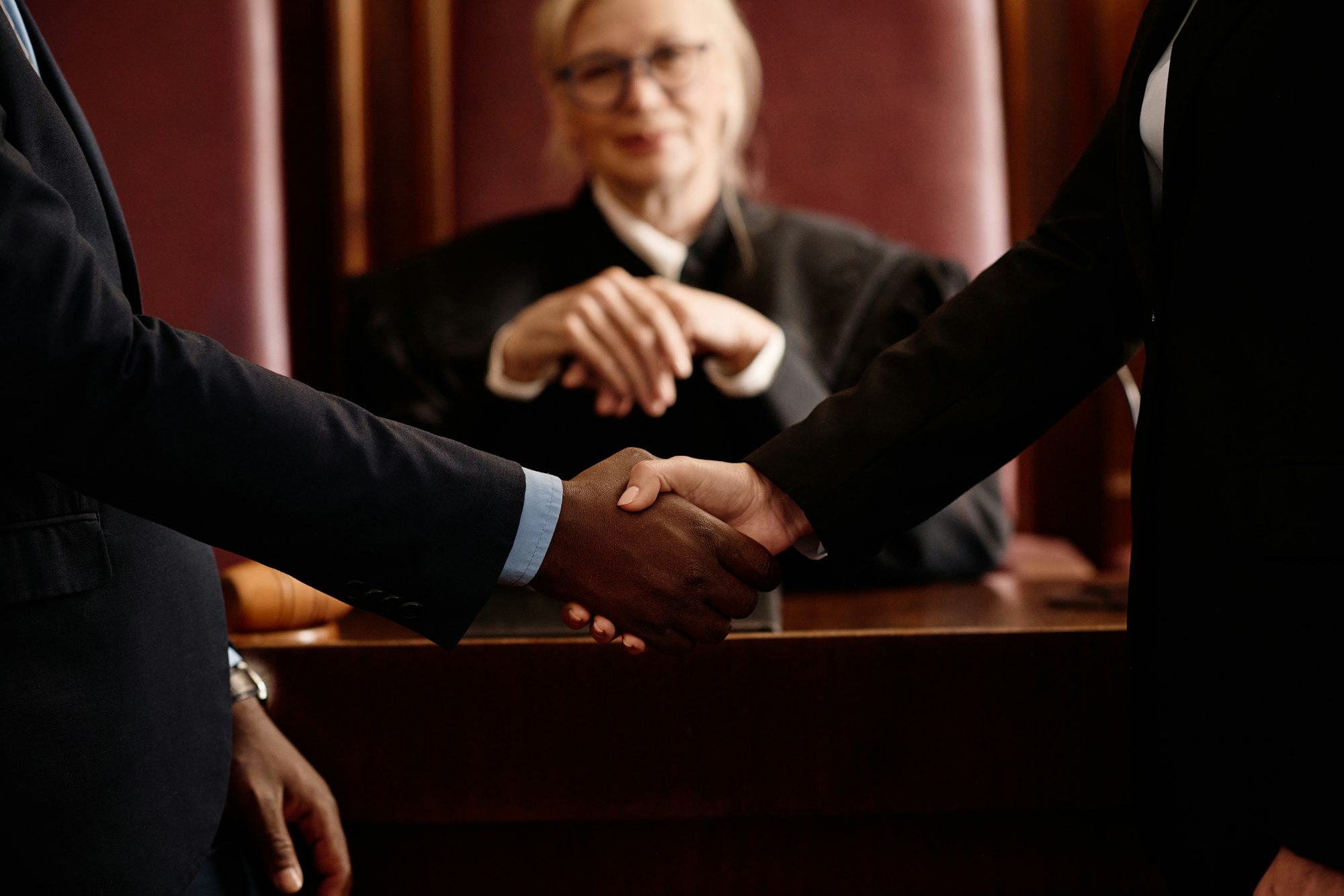 Close-up of two opposite sides of court case shaking hands against judge